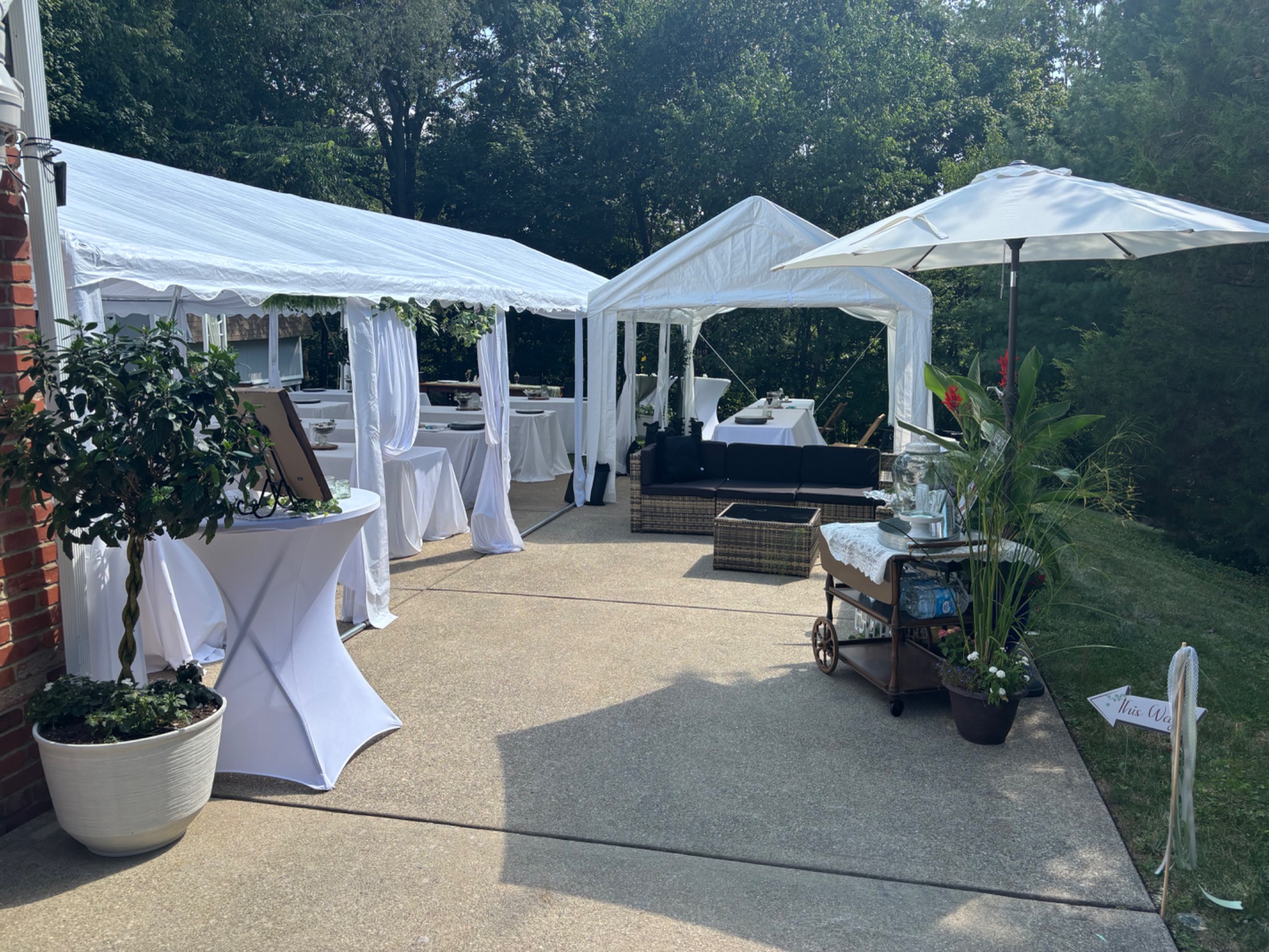 Backyard celebration with white draped tents, covered tables, lounge seating, a patio umbrella and a tea cart