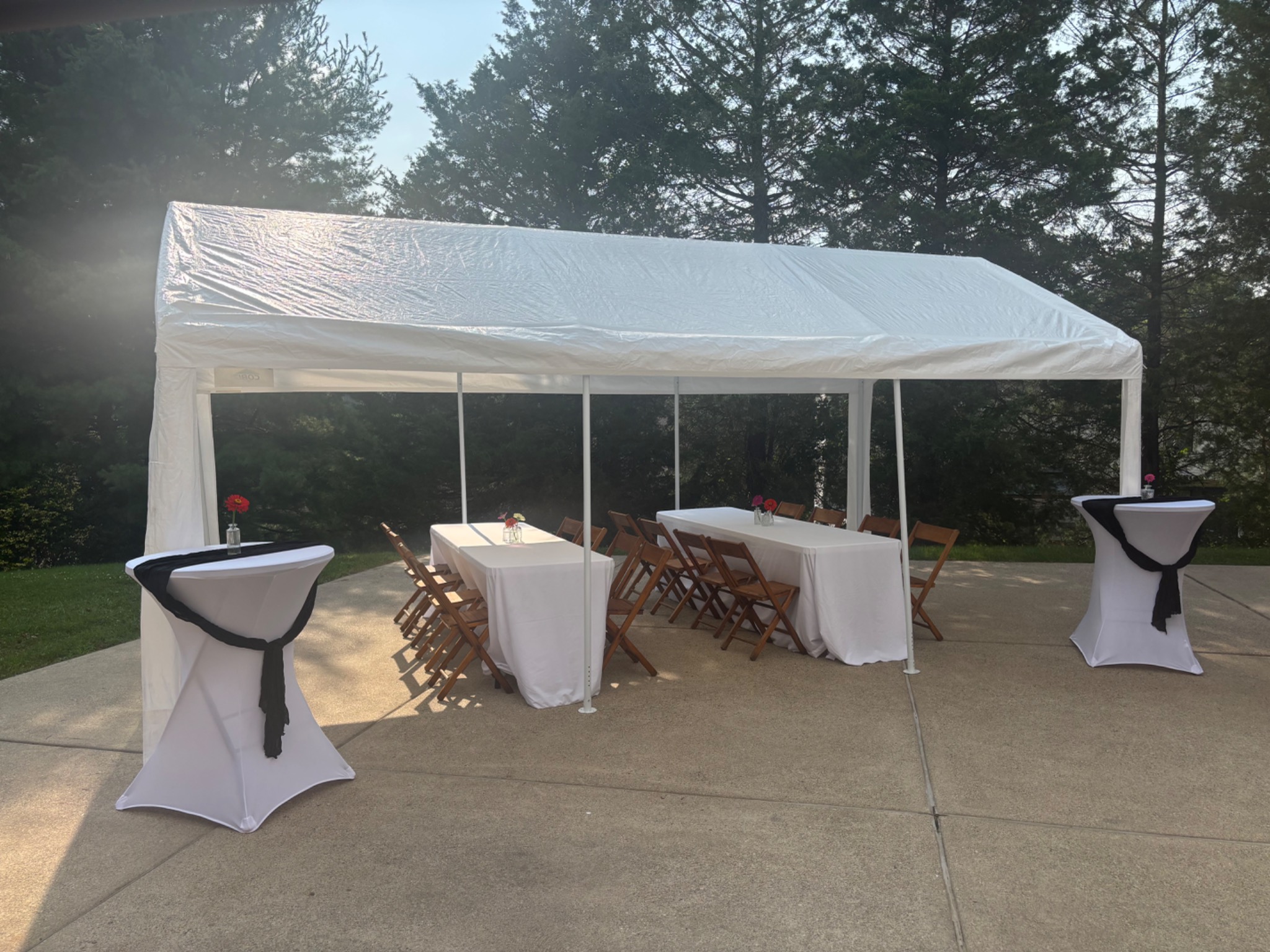 White party tent with three linen-covered tables, wooden folding chairs and two cocktail tables set up on a driveway