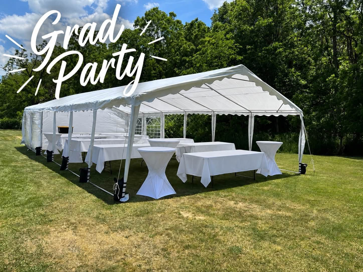 Graduation party setup with a white tent, covered tables and cocktail tables on a lawn