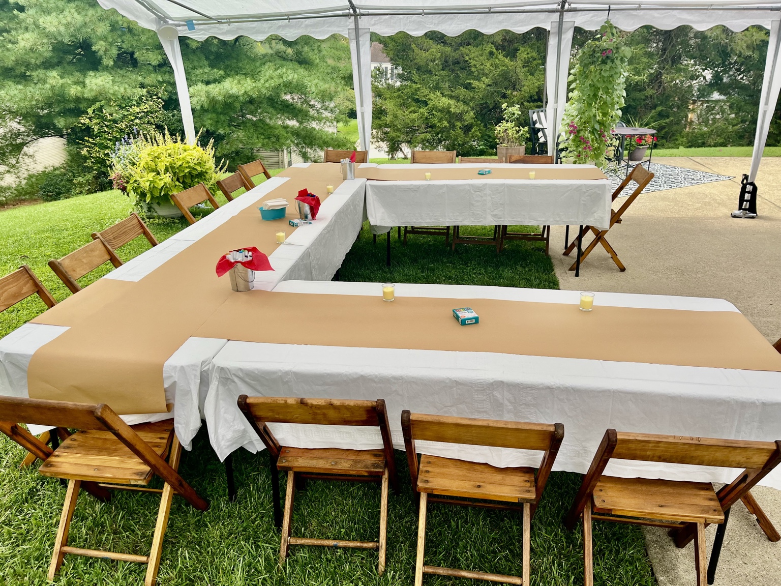 Covered outdoor seating with white table linens, tan runners and wooden chairs beneath a white tent