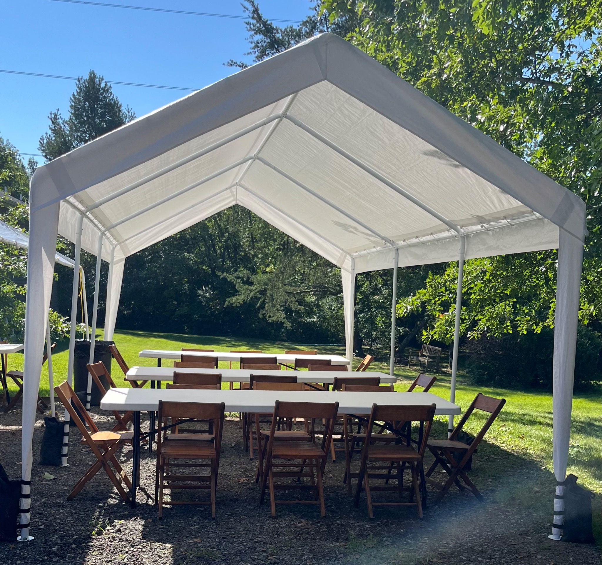 White backyard tent with tables and wooden folding chairs arranged beneath it