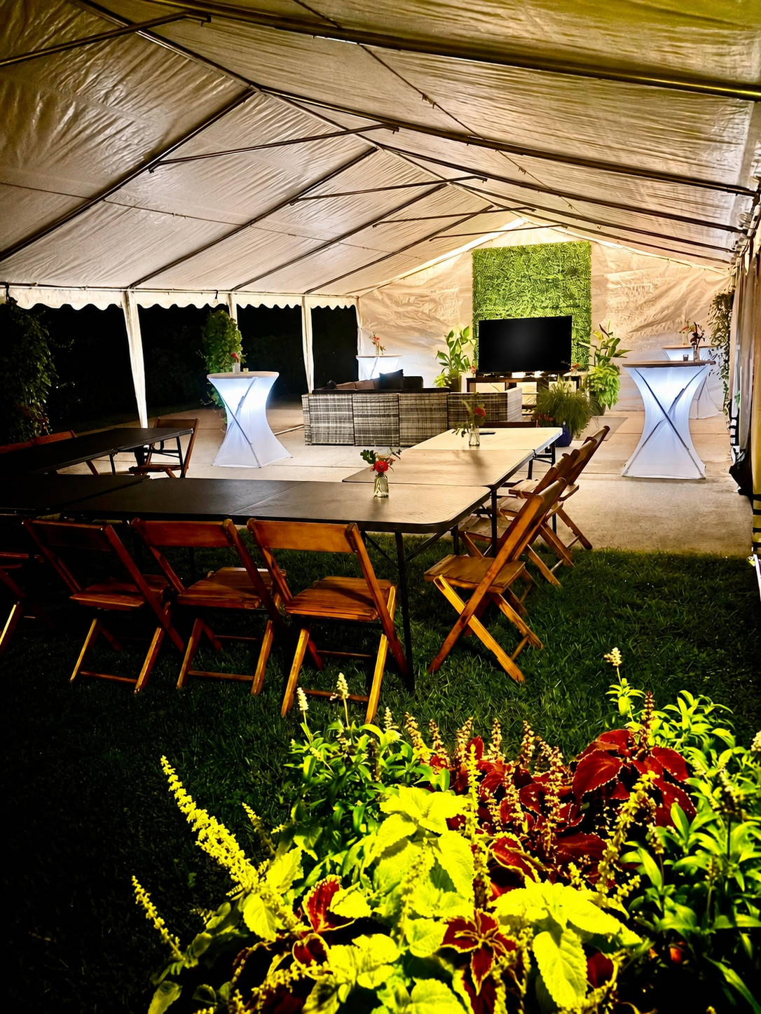 Large party tent with tables, chairs, lounge seating and greenery wall at night
