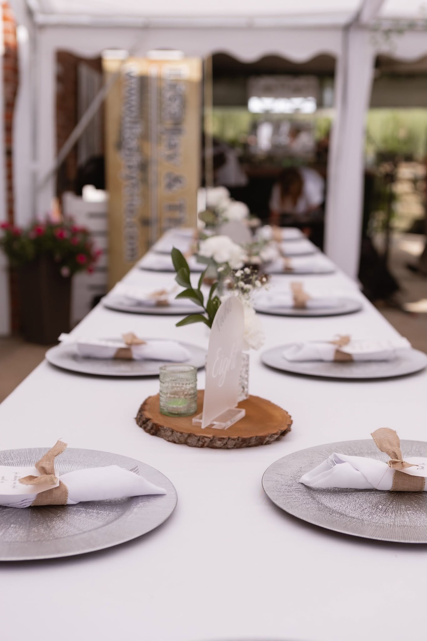Finished event table with white linens, silver charger plates, napkins, flowers, votive candle and custom sign